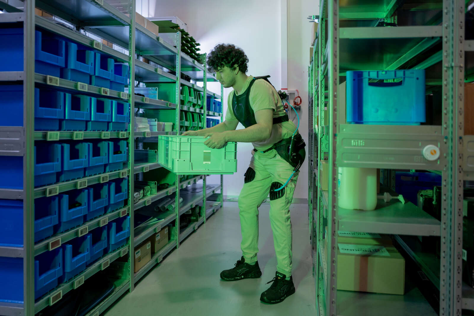 Mann trägt Exoskelett eine Kiste und steht vor Regal